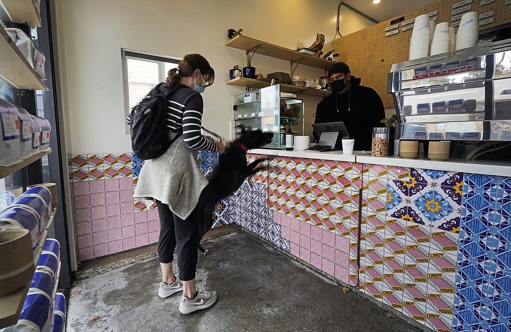 Natalie Sparrow with her dog, Jimmy John, orders her daily coffee to go at Collage Cafe in the Highland Park neighborhood of Los Angeles, Saturday, Nov. 6, 2021. A vaccine mandate that is among the strictest in the country takes effect Monday, Nov. 8, in Los Angeles, requiring proof of shots for everyone entering a wide variety of businesses from restaurants to shopping malls and theaters to nail and hair salons. (AP Photo/Damian Dovarganes)