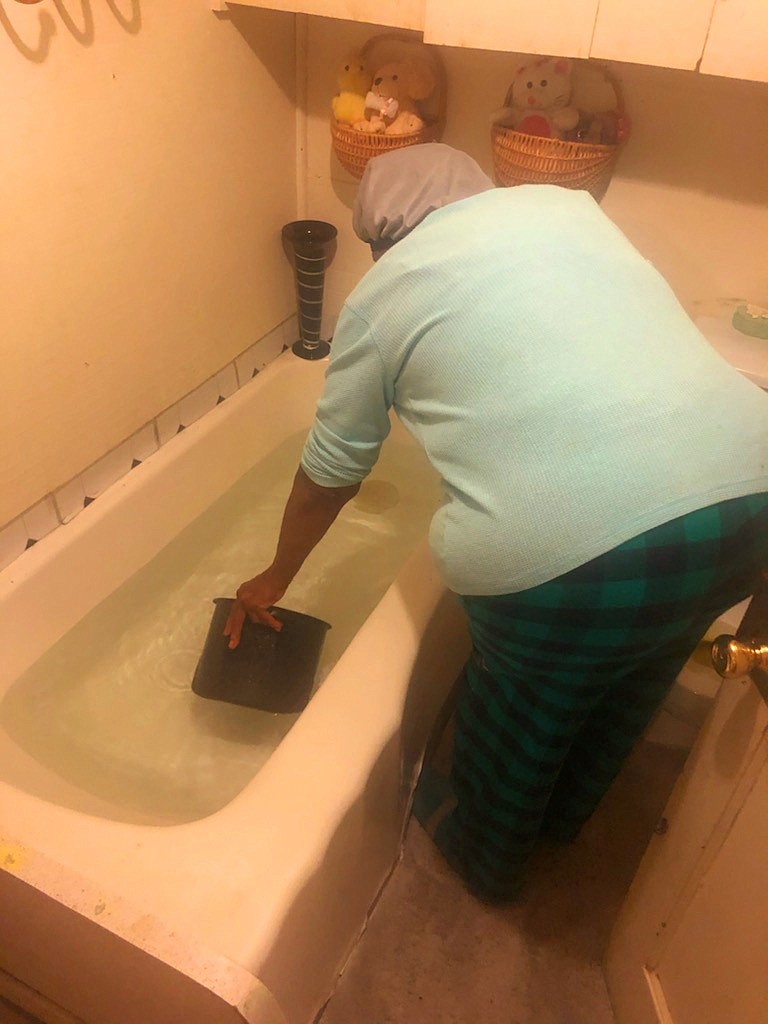 Gloria Harris, who does not have running water due to burst pipes from February's storm, scoops store-bought water she keeps filled in her tub into a cooking pot. (Special to the Commercial)