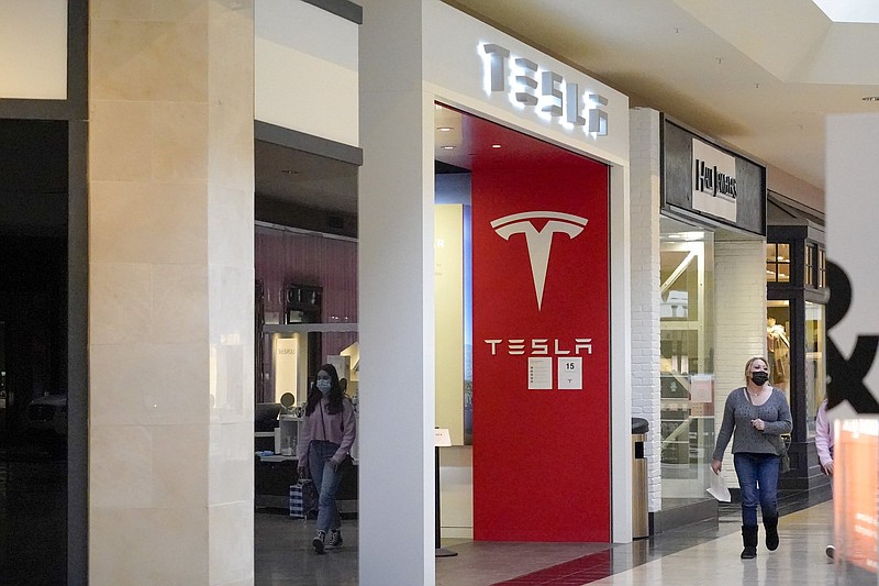 This photo made Wednesday, Feb. 24, 2021, shows people walking by the entrance to a Tesla store at a shopping mall in Pittsburgh. Tesla shares slumped about 5% in premarket trading after its CEO Elon Musk said he would sell 10% of his holdings ? about $20 billion worth ? in the electric car maker based on the results of a poll he conducted on Twitter over the weekend. (AP Photo/Keith Srakocic)