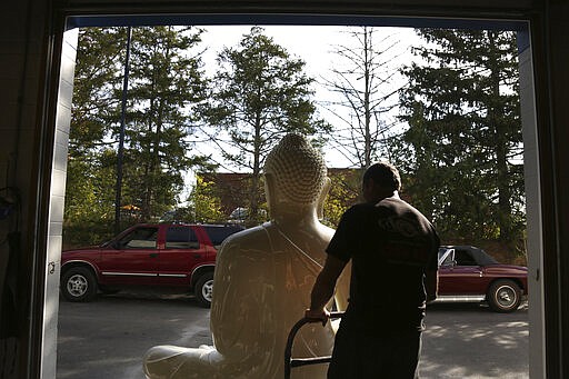 Dave Ley, co-owner of Exoticars, an auto restoration shop specializing in classic vehicles, pulls a newly restored statue of the Buddha inside the garage in McCandless, Pa., on Monday, Oct. 11, 2021. Workers repainted and repaired the figure for the Pittsburgh Buddhist Center, which brought it from Sri Lanka over 15 years ago. (AP Photo/Jessie Wardarski)