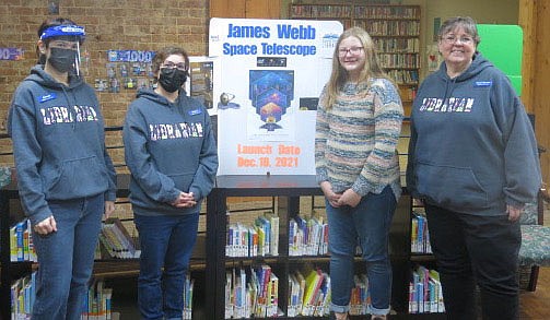 Westside Eagle Observer/SUSAN HOLLAND
Library clerks Artemis Edmondson and Brittany Mangold, Allie Cook and library director Karen Benson pose with a poster giving information about the James Webb Space Telescope to be launched next month in French Guiana. Cook, a seventh grader at Gravette Middle School, is volunteer at the library and helped with the Moon Over Main Street event.