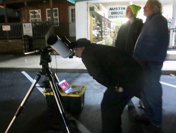 Westside Eagle Observer/SUSAN HOLLAND
Jocelyn Miller (center), of Gravette, and her father gaze up at the night sky as her mother looks through one of the telescopes set up at the Gravette Public Library's Moon Over Main Street event Saturday evening. The entire Miller family came out to enjoy the activities as part of the NASA@MyLibrary space science program.