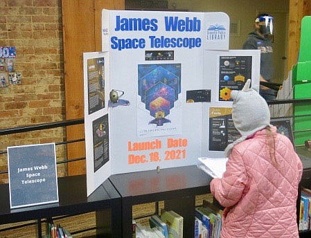 Westside Eagle Obsever/SUSAN HOLLAND
Kailee Miller, 6, of Gravette, looks over a poster displaying information about the James Webb Space Telescope to be launched Dec. 18 in French Guiana. The telescope will employ infrared technology and will take sharper images than the Hubble Telescope currently in orbit. The display was exhibited as part of the Gravette library's Moon Over Main Street event.