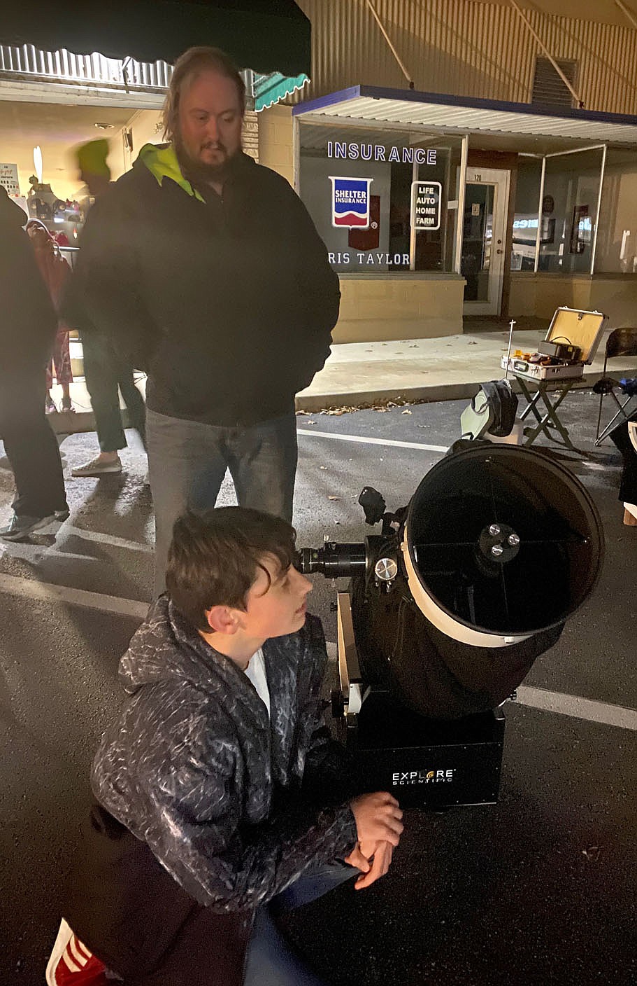 Submitted Photo
John Fare III, 12, of Gravette, views the moons of Jupiter through a telescope set up on Gravette Main Street Saturday evening while his father, John Fare, Jr., looks on. The father and son were among about 70 people who attended the Gravette Public Library's Moon Over Main Street event and enjoyed the various activities.