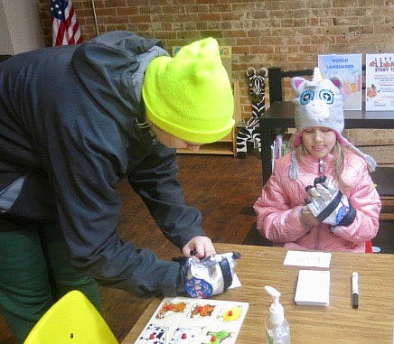 Westside Eagle Observer/SUSAN HOLLAND
Jocelyn Miller tries writing her name while wearing NASA issued gloves like the astronauts wear when on a space mission while her little sister Kailee, age 6, tries one of the gloves on for size. The girls were getting the feel of how tasks are performed in space while in full flight gear. The activity was a part of the Gravette library's Moon Over Main Street event.