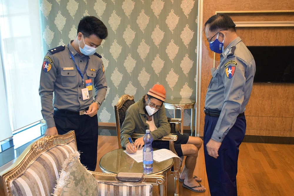 In this photo provided by the Myanmar Military True News Information Team, released American journalist Danny Fester writes on a document while seated between two police officers at the Naypyitaw International Airport in Naypyitaw, Myanmar Monday, Nov. 15, 2021. Fenster, who was recently sentenced to 11 years of hard labor after spending nearly six months in jail in military-ruled Myanmar, has been freed. A former U.S. diplomat who helped negotiate the release said Fenster was on his way home Monday. (Myanmar Military True News Information Team via AP)