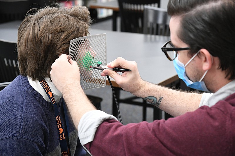 Brett Williams, right, teen librarian, paints a dragon design on fellow Garland County Library employee Laura Hill’s face at Magical Creatures Night on Friday. It was one of the first in-person events at the library since the pandemic started. - Photo by Tanner Newton of The Sentinel-Record