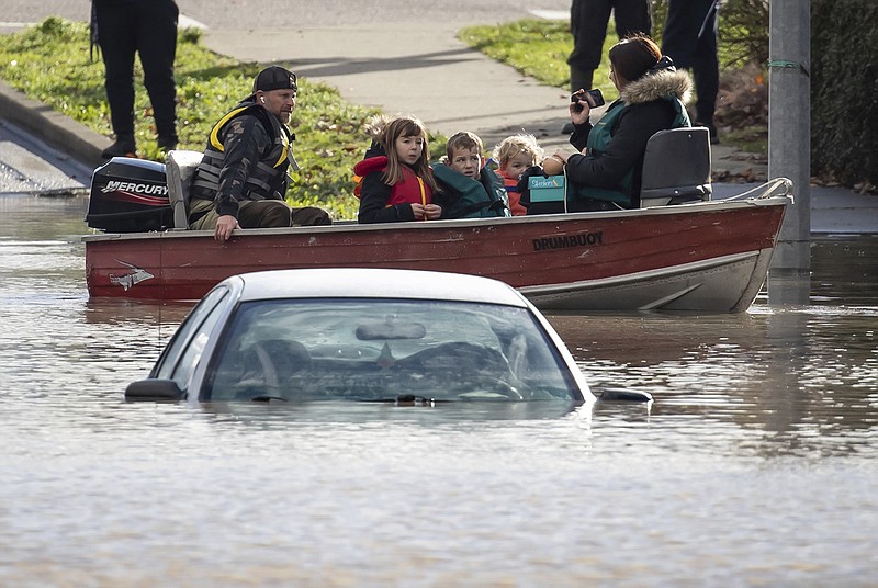 A woman and children who were stranded by high water due to flooding are rescued by a volunteer operating a boat as another person's car is submerged near them in Abbotsford, British Columbia, on Tuesday, Nov. 16, 2021. (Darryl Dyck/The Canadian Press via AP)