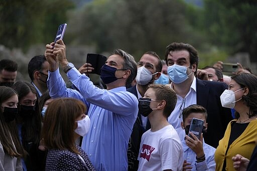 Greece's Prime Minister Kyriakos Mitsotakis, center, and school students use a mobile app at the ancient site of Olympia, southwestern Greece, Wednesday, Nov. 10, 2021. Microsoft launched a digital restoration project at the ancient birthplace of the Olympic Games in southern Greece Wednesday to provide visitors an immersive recreation of temples and competition areas as they walk through the ruins. (AP Photo/Thanassis Stavrakis)