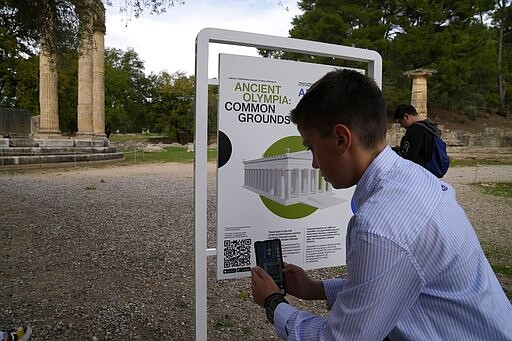 A school student scans a QR code at the ancient site of Olympia, southwestern Greece, Wednesday, Nov. 10, 2021. Microsoft launched a digital restoration project at the ancient birthplace of the Olympic Games in southern Greece Wednesday to provide visitors an immersive recreation of temples and competition areas as they walk through the ruins. (AP Photo/Thanassis Stavrakis)