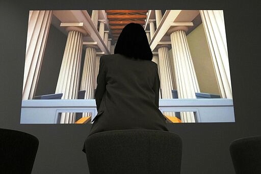 Museum supervisor Xenia Vlahou watches a video projection of Ancient Olympia temple at the Olympic Museum in Athens, Greece, Tuesday, Nov. 9, 2021. The installation is part of a digital restoration project by Microsoft and the Greek Ministry of Culture and Sport at Ancient Olympia, birthplace of the Olympic Games. (AP Photo/Thanassis Stavrakis)