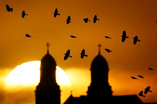 FILE - A flock of birds fly past a Catholic church as the sun rises Thursday, Jan. 14, 2021, in Damar, Kan.  For many Christians, the relationship between birds and faith does not stray farther than seeing a dove carrying an olive branch on a banner at church. However, for Christian birdwatchers &#x2014; or to use a phrase coined by theologian John Stott, &#x201c;ornitheologists&#x201d; &#x2014; birding is a kind of worship.  (AP Photo/Charlie Riedel, File)