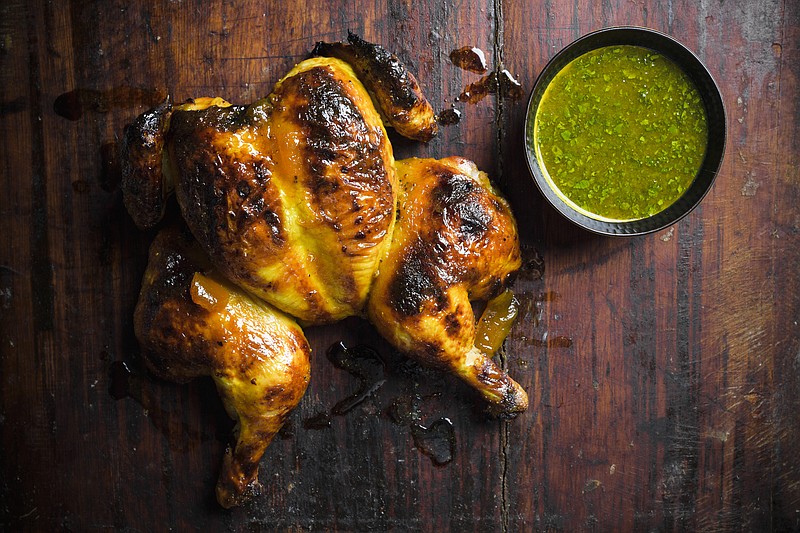 This image released by Milk Street shows a recipe for chutney-glazed spatchcocked chicken. Spatchcocking, or butterflying, involves cutting out a bird&#x2019;s backbone so it can be flattened. This allows the chicken to brown evenly and helps the glaze stay put. Their simple glaze mixes tangy-sweet chutney with butter and turmeric. Citrus juice added to a portion of the glaze before cooking makes a bright dipping sauce. (Milk Street via AP)