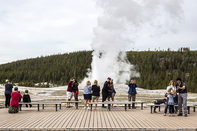 FILE - In this May 18, 2020, file photo, visitors watch as Old Faithful erupts at Yellowstone National Park, Wyo.  Americans may soon get a better glimpse into a future of green-friendly transportation by visiting a U.S. national park. It&#x2019;s a joint pledge being signed Wednesday by Interior Secretary Deb Haaland and Transportation Secretary Pete Buttigieg to test some of the newest and most innovative travel technologies on public lands. The plan is being made possible by the $1 trillion infrastructure law and other federal spending. Under new pilot programs, visitors to national parks could see self-driving shuttle buses, along with more electric scooter or bike stations and electric charging stations for travelers in zero-emission cars. Yellowstone National Park would see some of the most immediate updates, with other sites to follow.  (Ryan Dorgan/Jackson Hole News &amp; Guide via AP, File)