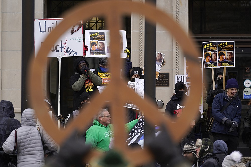 Protesters, framed by a peace symbol, stand outside the Kenosha County Courthouse, Thursday, Nov. 18, 2021 in Kenosha, Wis., during the Kyle Rittenhouse murder trial. Rittenhouse is accused of killing two people and wounding a third during a protest over police brutality in Kenosha last year. (AP Photo/Paul Sancya)