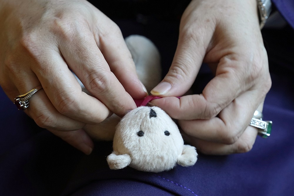 A Massachusetts resident identifying herself only as "Safi," who asked that her last name not be used for fear of retribution against her relatives in Afghanistan, ties a bow around a keepsake teddy bear Tuesday, Nov. 9, 2021, during an interview with The Associated Press. Thousands of Afghans have applied for temporary admission into the U.S. for humanitarian reasons, but few have been approved since the Taliban recaptured control of their homeland. "We're worried for their lives," said Safi, whose family is sponsoring some 20 other relatives seeking humanitarian parole. (AP Photo/Steven Senne)