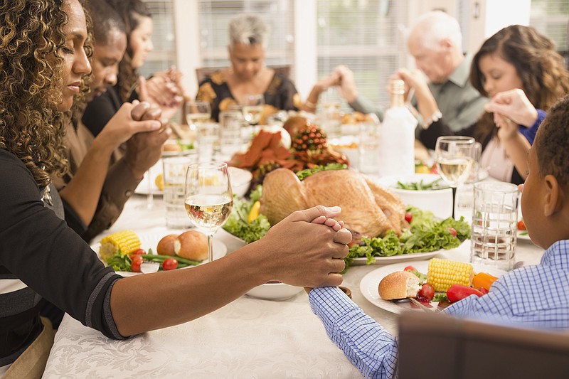 Multi-ethnic family and friends pray during Thanksgiving dinner. Close-up of hands in foreground.