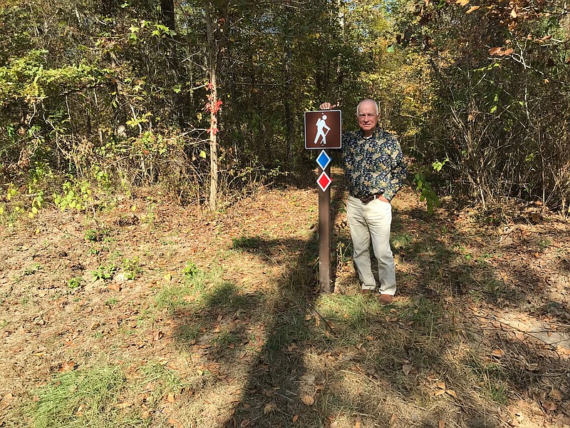 Joe Stuckey, one of several volunteers who helps improve and maintain Alex Smith Park, in Miller County, stand near a walking trail identification post close to where of the trails connect. Each trail has its own color code as displayed the post. (Staff Photo By Greg Bischof)