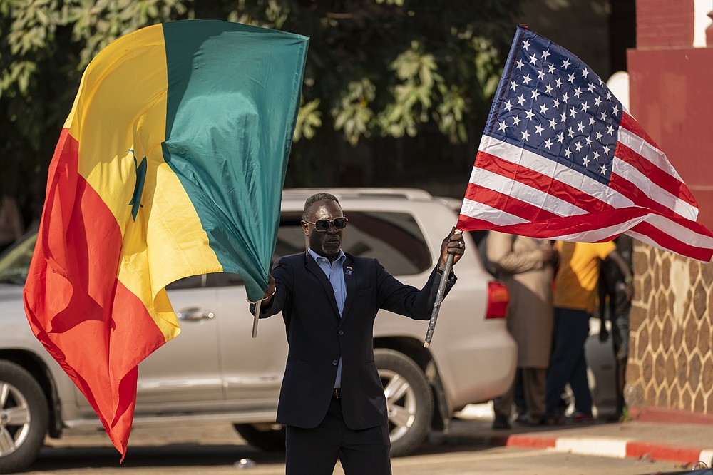 A man waves a Senegalese and an American flag as the motorcade carrying Secretary of State Antony Blinken prepares to leave the Ministry of Foreign Affairs in Dakar, Senegal, Saturday, Nov. 20, 2021. Blinken is on a five day trip to Kenya, Nigeria, and Senegal. (AP Photo/Andrew Harnik, Pool)