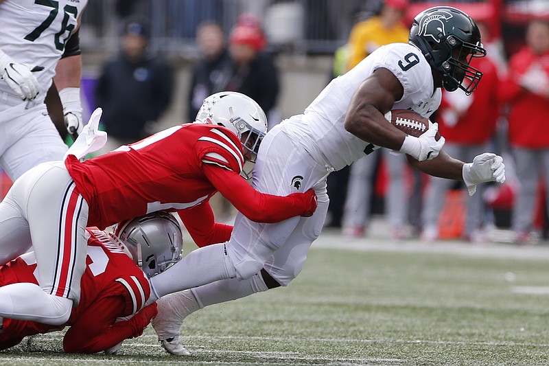 Ohio State defensive back Cameron Brown, bottom, and defensive back Bryson Shaw, center, tackle Michigan State running back Kenneth Walker during the first half of an NCAA college football game Saturday, Nov. 20, 2021, in Columbus, Ohio. (AP Photo/Jay LaPrete)