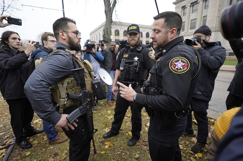 Kenosha County Sheriffs Department officers question a protester carrying a rifle outside the Kenosha County Courthouse, Wednesday, Nov. 17, 2021 in Kenosha, Wis., during the Kyle Rittenhouse murder trial. Rittenhouse is accused of killing two people and wounding a third during a protest over police brutality in Kenosha, last year. (AP Photo/Paul Sancya)