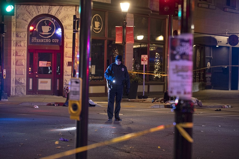 A police officer uses a flashlight while looking for evidence in downtown Waukesha, Wis., after an SUV sped through a barricade and slammed into a Christmas parade, injuring multiple people Sunday, Nov. 21, 2021. (AP Photo/Jeffrey Phelps)