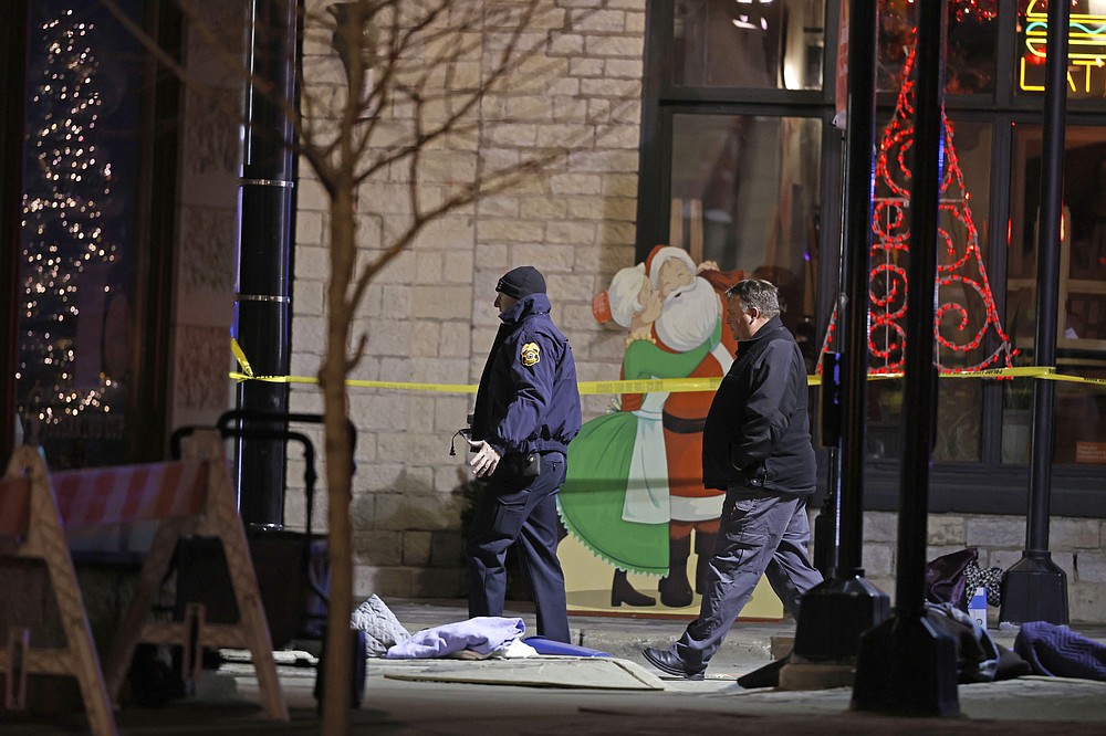 Holiday decorations frame police investigators in downtown Waukesha, Wis., after an SUV plowed into a parade of Christmas marchers, killing multiple people Sunday, Nov. 21, 2021. (AP Photo/Jeffrey Phelps)