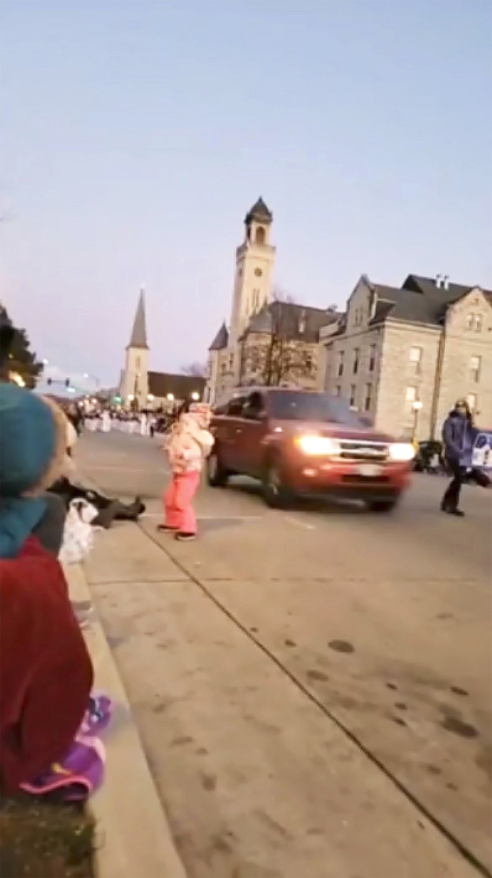 In this image taken from video an SUV speeds past a young girl and others attending a Christmas parade and continues to drive through the parade, injuring multiple people, Sunday, Nov. 21, 2021, in Waukesha, Wis. (Jesus Ochoa via AP)
