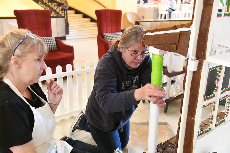 Carmen Jones, right, director of operations at the Arlington Resort Hotel & Spa, applies melted Jolly Ranchers onto the gingerbread house in the hotel’s lobby as Melanie Hancock assists. - Photo by Tanner Newton of The Sentinel-Record