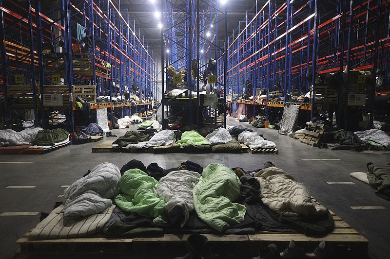 Migrants sleep a logistics center at the checkpoint "Kuznitsa" at the Belarus-Poland border near Grodno, Belarus, Monday, Nov. 22, 2021. Belarus President Alexander Lukashenko on Monday chafed at the European Union for its refusal to hold talks on the influx of migrants on the country's border with Poland and urged Germany to accommodate about 2,000 migrants who had remained on the border with Poland. (Maxim Guchek/BelTA via AP)