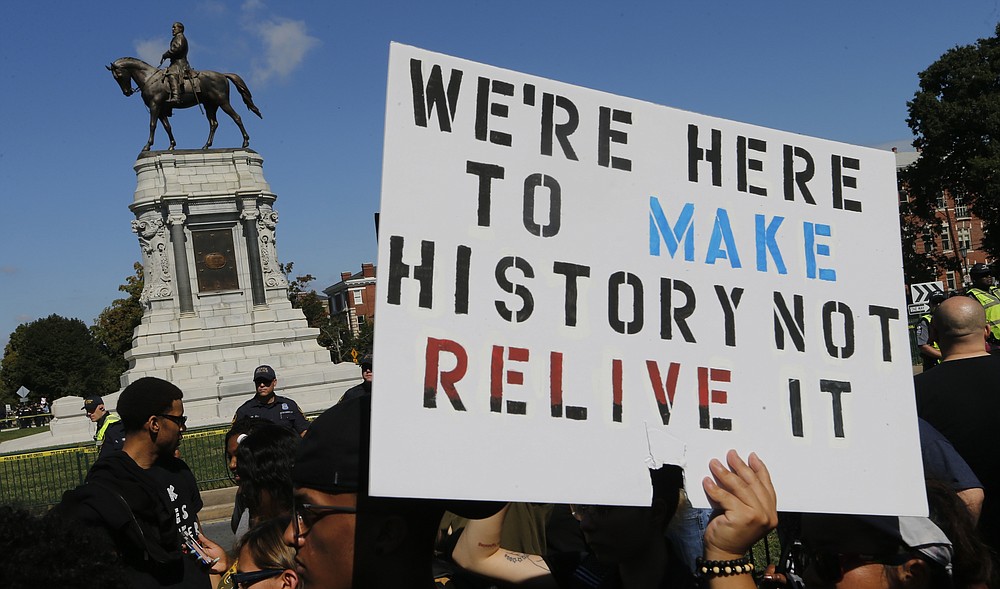 FILE - In this Saturday, Sept. 16, 2017 file photo, protesters hold signs in front of the statue of Confederate General Robert E. Lee on Monument Avenue in Richmond, Va. A jury began deliberations Friday, Nov. 19, 2021 in a civil trial of white nationalists accused of conspiring to commit racially motivated violence at the deadly “Unite the Right" rally in Charlottesville four years ago.(AP Photo/Steve Helber, File)
