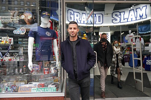 David Cohen, an owner of Grand Slam, a souvenir and sports apparel store, poses for a picture at the store in Times Square, Monday, Nov. 15, 2021, in New York. Even as visitors again crowd below the jumbo screens in New York’s Times Square, the souvenir shops, restaurants, hotels and entrepreneurs within the iconic U.S. landmark are still reeling from a staggering pandemic. (AP Photo/Seth Wenig)