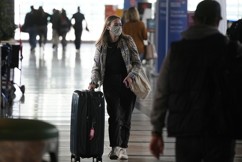 A traveller wears a face covering while heading to the American Airlines check-in counter as the Thanksgiving Day holiday approaches Tuesday, Nov. 23, 2021, at Denver International Airport in Denver. Last year with the pandemic raging, travelers were urged to stay home. Not this year. With more people vaccinated, expect to see busier roads and airports as family and friends gather again for Thanksgiving and the December holidays. (AP Photo/David Zalubowski)