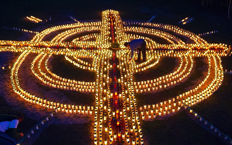 FILE - A woman lights candles forming a giant cross in memory of coronavirus victims in Germany in Zella-Mehlis, Germany, April 17, 2020. Germany is set to mark 100,000 deaths from COVID-19 this week, passing a somber milestone that several of its neighbors crossed months ago but which some in Western Europe's most populous nation had hoped to avoid. (AP Photo/Jens Meyer, File)