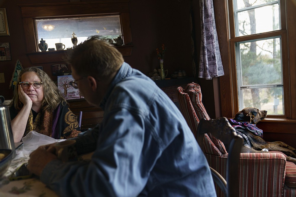 Caroline Clarin, right, talks with her wife, Sheril Raymond, as their dog, Iorek, looks out the window at their home in Dalton, Minn., Tuesday, Oct. 26, 2021. Raymond worries more than Clarin about money they've spent to bring families over from Afghanistan, and she finds the government fee of $575 per application for humanitarian parole outrageous. But she also acknowledges they cannot step back now. "When we bring in a family, they become our family," she said. (AP Photo/David Goldman)