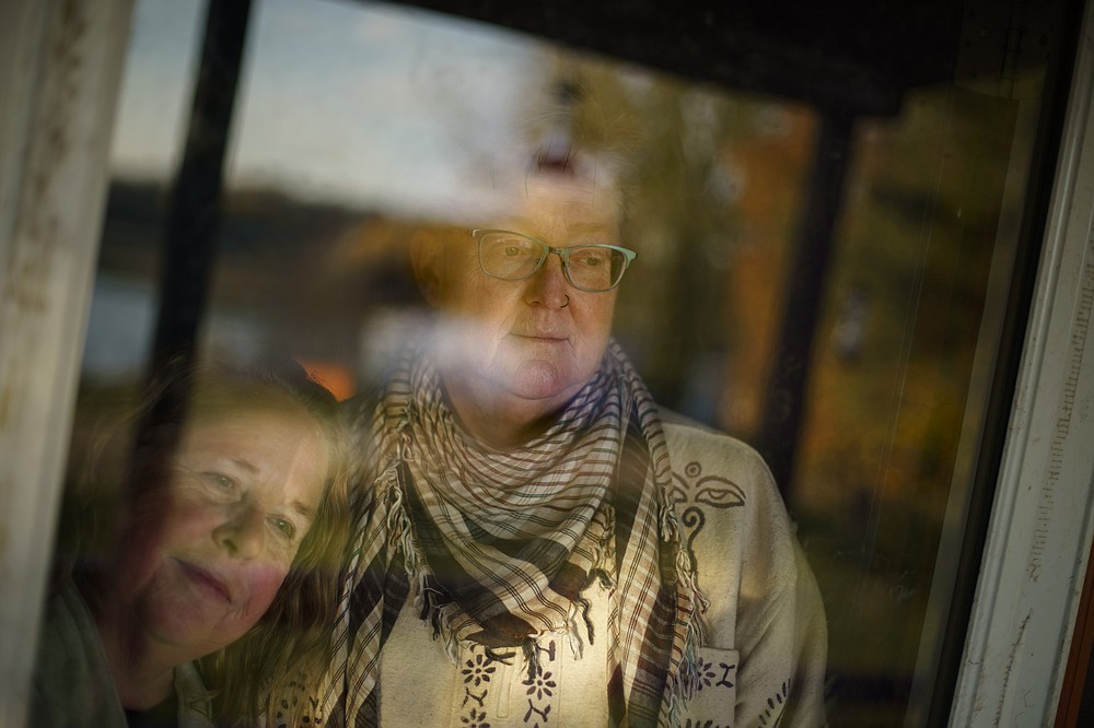 Sheril Raymond, left, and her wife, Caroline Clarin, look out from their front door in Dalton, Minn., Thursday, Oct. 28, 2021. When Clarin was in Afghanistan, it was the longest she and Raymond had been apart since they started dating in 1988. Raymond, who cares for the chickens, pigs and other animals on their farm, would do video calls often, staying online even after Clarin had fallen asleep. Two years after Clarin returned, they married in August 2013 when same-sex marriage became legal in Minnesota. (AP Photo/David Goldman)