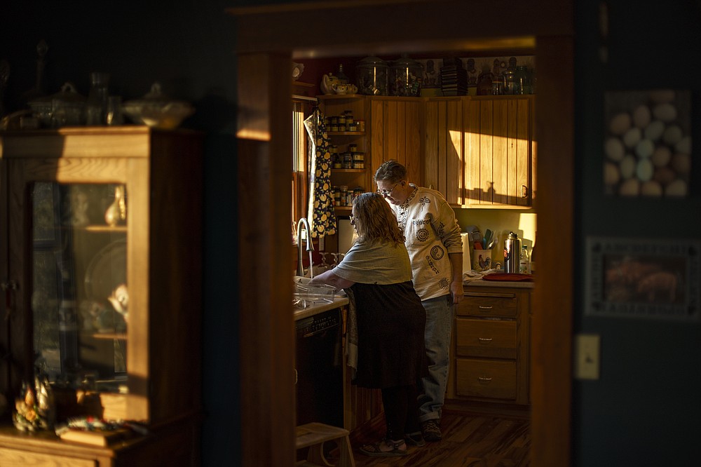 Caroline Clarin, right, and her wife, Sheril Raymond, prepare dinner at their home in Dalton, Minn., Thursday, Oct. 28, 2021. So far, the couple has spent just under $10,000 since May bringing over families from Afghanistan. Raymond keeps the tally in a notebook. "It does make me a little nervous because we've lived on the edge for so long," said Raymond, who sews her dresses, knits hats, and bakes bread. "So I work another year before retiring," Clarin, 55, answers with a shrug. (AP Photo/David Goldman)