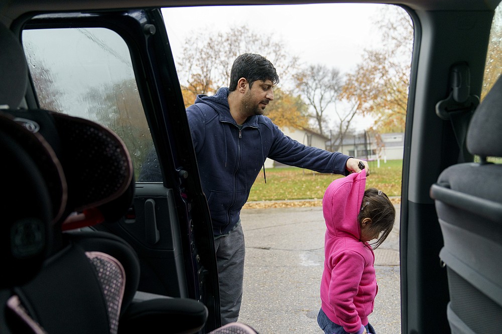 Ihsanullah Patan, a horticulturist and refugee from Afghanistan, puts the hood up for his daughter, Sujda, 5, after picking her up from daycare in Fergus Falls, Minn., Wednesday, Oct. 27, 2021. Only months after they arrived, the Patan family already feels at home. "In Fergus Falls, they have really good people, really friendly people," Patan said as he drove his minivan down the tree-lined streets. (AP Photo/David Goldman)