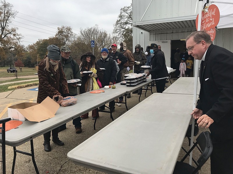 The Rev. Richard R. Daly (right) of the St. James Episcopal Church, adjusts a table while Randy Sams Outreach Shelter residents line up for the shelter's annual free Thanksgiving dinner Thursday. Serving the annual holiday dinner has now been a tradition of the shelter for more than 20 years (Staff Photo By Greg Bischof)