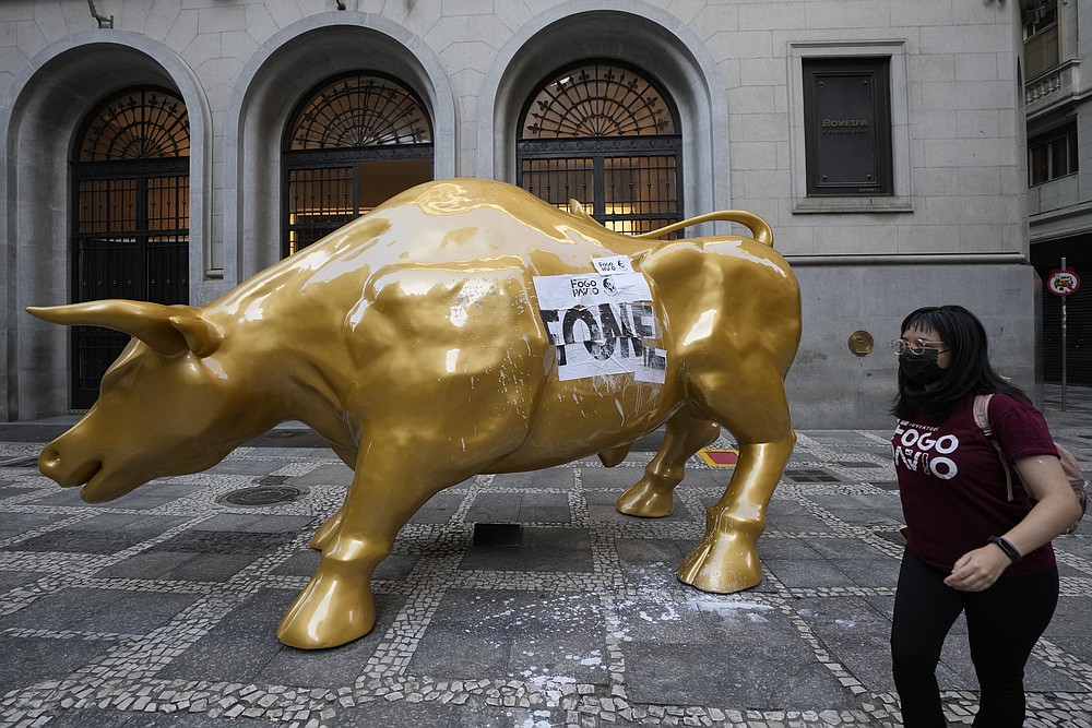 An activists walks past the Golden Bull, a replica of Wall street Charging Bull symbolizing the financial market, after her group pasted the Portuguese word &amp;quot;hungry&amp;quot; on it, outside the Brazilian B3 Stock Exchange in Sao Paulo, Brazil, Wednesday, Nov. 17, 2021. (AP Photo/Andre Penner)