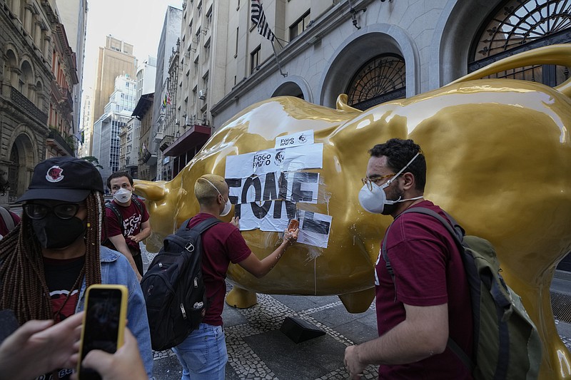 Activists paste the Portuguese word &quot;hungry&quot; on the Golden Bull, a replica of Wall street Charging Bull symbolizing the financial market, outside the Brazilian B3 Stock Exchange in Sao Paulo, Brazil, Wednesday, Nov. 17, 2021. (AP Photo/Andre Penner)