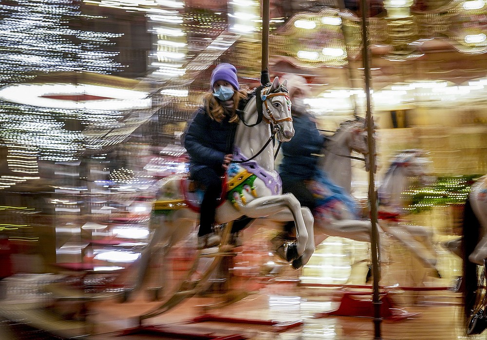 FILE - A girl rides on a merry-go-round on the first day of the Christmas market in Frankfurt, Germany, Monday, Nov. 22, 2021. Despite the pandemic inconveniences, stall owners selling ornaments, roasted chestnuts and other holiday-themed items in Frankfurt and other European cities are relieved to be open at all for their first Christmas market in two years, especially with new restrictions taking effect in Germany, Austria and other countries as COVID-19 infections hit record highs. (AP Photo/Michael Probst, File)