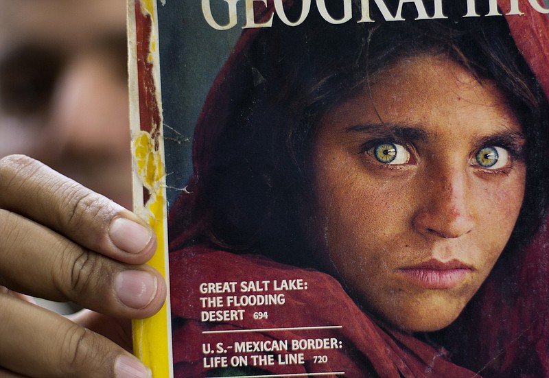 FILE - In this file photo taken on Oct. 26, 2016, Pakistan's Inam Khan, owner of a book shop shows a copy of a magazine with the photograph of Afghan refugee woman Sharbat Gulla, from his rare collection in Islamabad, Pakistan. National Geographic&#x2019;s famed green-eyed &#x201c;Afghan Girl&#x201d; has arrived in Italy as part of the West&#x2019;s evacuation of Afghans following the Taliban takeover of the country, the Italian government said Thursday. The office of Premier Mario Draghi said Italy had organized the evacuation of Sharbat Gulla after she asked to be helped to leave the country. The Italian government will now help to welcome her and get her integrated into life here, the statement said.(AP Photo/B.K. Bangash, File)