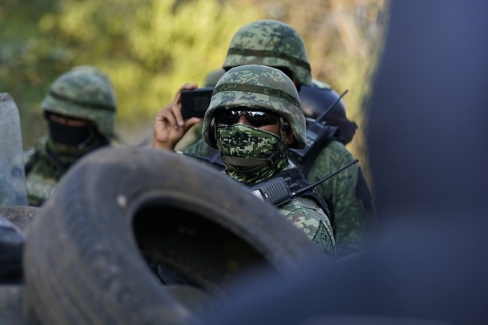 Mexican soldiers take cover behind a barricade of car tires against protesters who are fed up with the army’s strategy of simply separating the Jalisco and the Michoacan-based Viagras gangs, during a march against roadblocks in Loma Blanca, Mexico, Tuesday, Nov. 16, 2021. (AP Photo/Eduardo Verdugo)