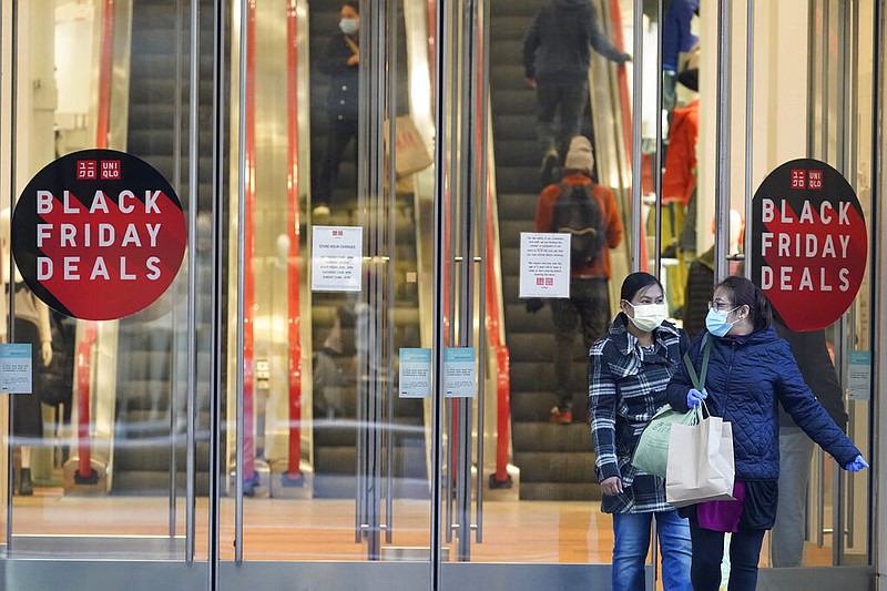 In this file photo, Black Friday shoppers wear face masks and gloves during the coronavirus pandemic as they leave the Uniqlo store along Fifth Avenue, Friday, Nov. 27, 2020, in New York. Retailers are expected to usher in the unofficial start to the holiday shopping season Friday, Nov. 26, 2021, with bigger crowds than last year in a closer step toward normalcy. But the fallout from the pandemic continues to weigh on businesses and shoppers' minds. (AP Photo/Mary Altaffer, File)
