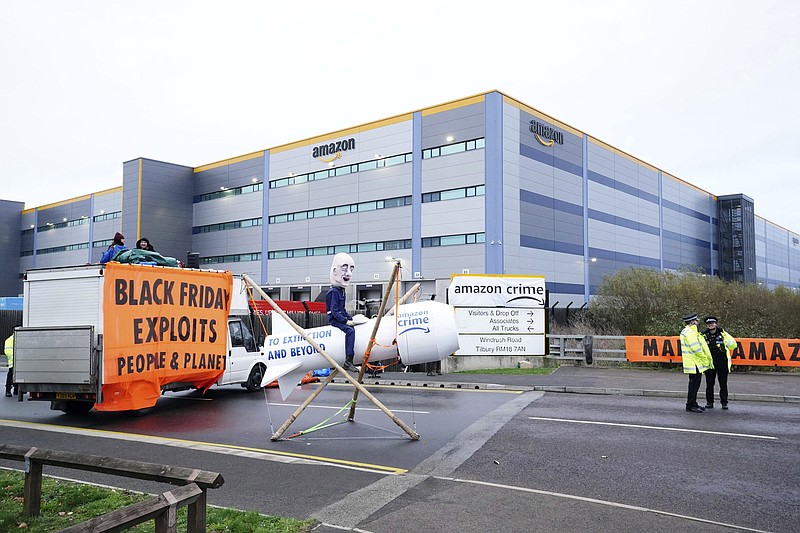 Activists from Extinction Rebellion block the entrance to the Amazon fulfilment centre, preventing lorries from entering or leaving on Black Friday, the global retail giant's busiest day of the year, in Tilbury, England,  Friday Nov. 26, 2021. The group has targeted Amazon sites in Doncaster, Darlington, Dunfremline, Newcastle, Manchester, Peterborough, Derby, Coventry, Rugeley, Dartford, Bristol, Tilbury and Milton Keynes. (Ian West/PA via AP)