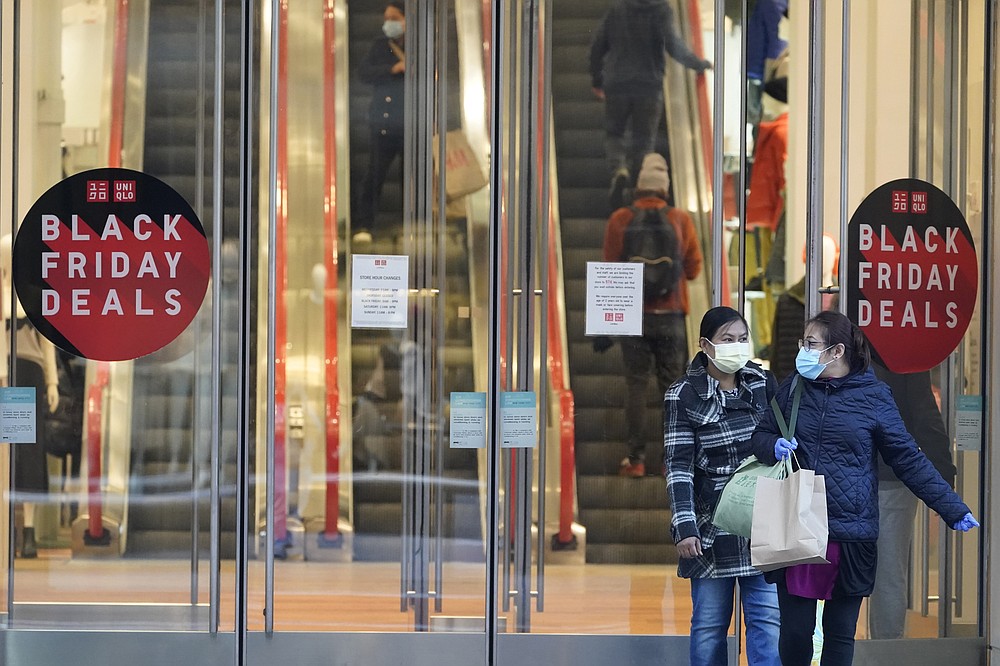 FILE - Black Friday shoppers wear face masks and gloves during the coronavirus pandemic as they leave the Uniqlo store along Fifth Avenue, Friday, Nov. 27, 2020, in New York. Retailers are expected to usher in the unofficial start to the holiday shopping season Friday, Nov. 26, 2021, with bigger crowds than last year in a closer step toward normalcy. But the fallout from the pandemic continues to weigh on businesses and shoppers&#x27; minds. (AP Photo/Mary Altaffer, File)