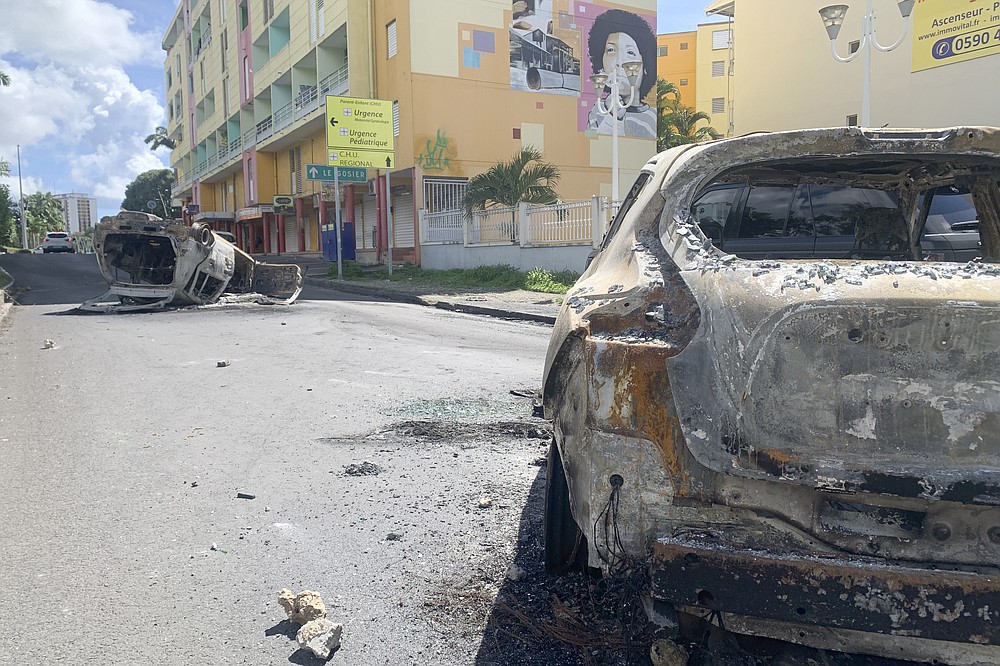 Charred car are pictured in a s street of Le Gosier, Guadeloupe island, Sunday, Nov.21, 2021. French authorities sent police special forces to the Caribbean island of Guadeloupe, an overseas territory of France, as protests over COVID-19 restrictions erupted into rioting and looting for the third day in a row. On Sunday, many road blockades by protesters made traveling across the island nearly impossible. (AP Photo/Elodie Soupama)