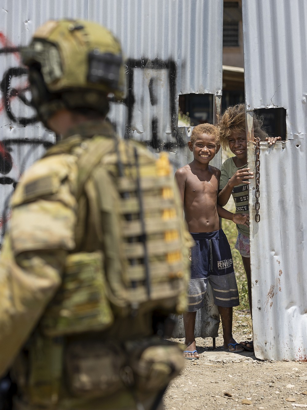 In this photo provided by the Department of Defence, Australian Army Corporal Aaron Woodham is watched by young boys during a community engagement patrol through Honiara, Solomon Islands, Saturday, Nov. 27, 2021. Solomon Islands police have found multiple bodies in a burned-out building and arrested more than 100 people in this week&#x27;s violence sparked by concerns about the Pacific nation&#x27;s increasing links with China. (Cpl. Brandon Grey/Department of Defence via AP)