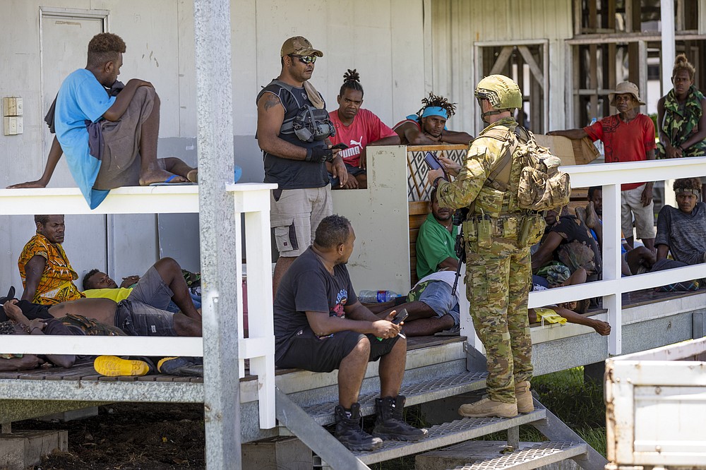 In this photo provided by Department of Defence, an Australian Army soldier talks with local citizens during a community engagement patrol through Honiara, Solomon Islands, Saturday, Nov. 27, 2021. Solomon Islands police have found multiple bodies in a burned-out building and arrested more than 100 people in this week&#x27;s violence sparked by concerns about the Pacific nation&#x27;s increasing links with China. (Cpl. Brandon Grey/Department of Defence via AP)